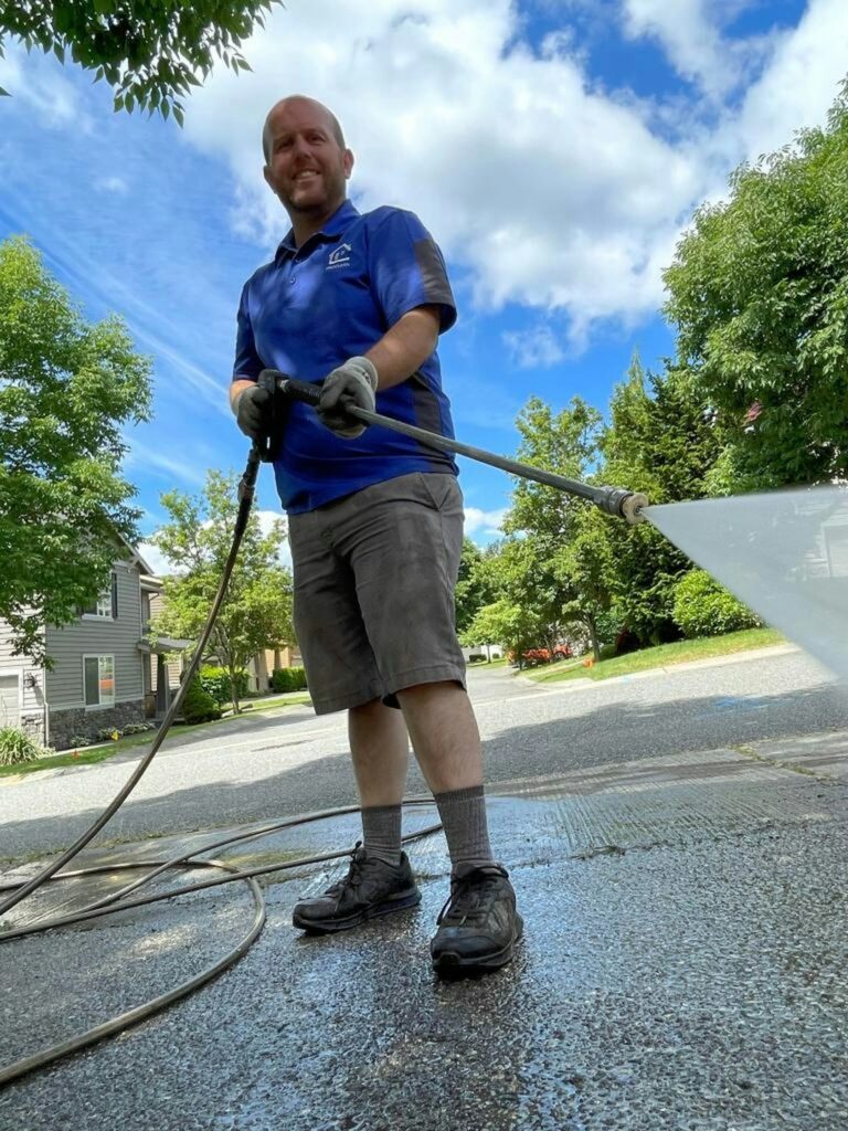 A person uses a pressure washer with a wide spray on a red brick house exterior.