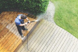 A homeowner preparing their patio by moving furniture and potted plants before exterior cleaning.