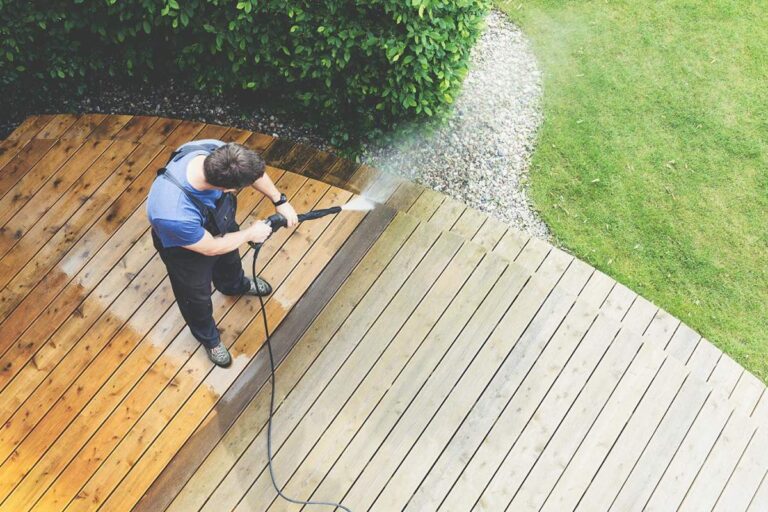 A homeowner preparing their patio by moving furniture and potted plants before exterior cleaning.