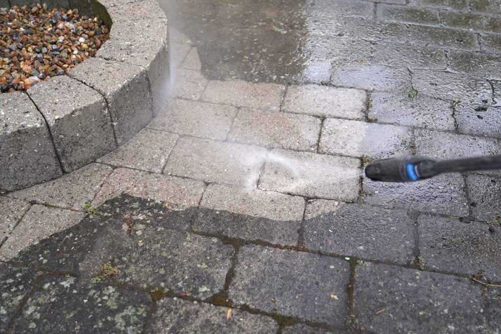 Technician cleaning a concrete walkway beside a bright residential entry with palms and outdoor walls.