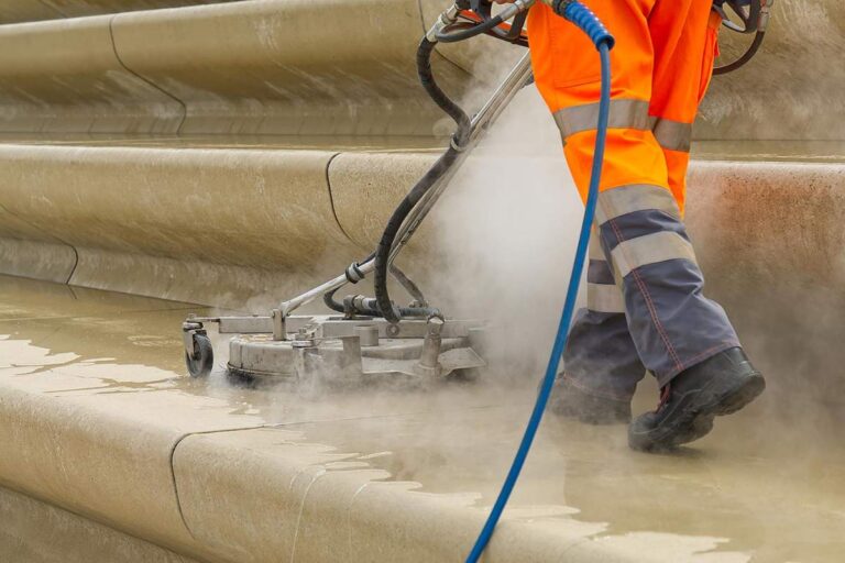 Professional cleaning equipment rinses a stained concrete patio beside outdoor furniture and landscaped surroundings.